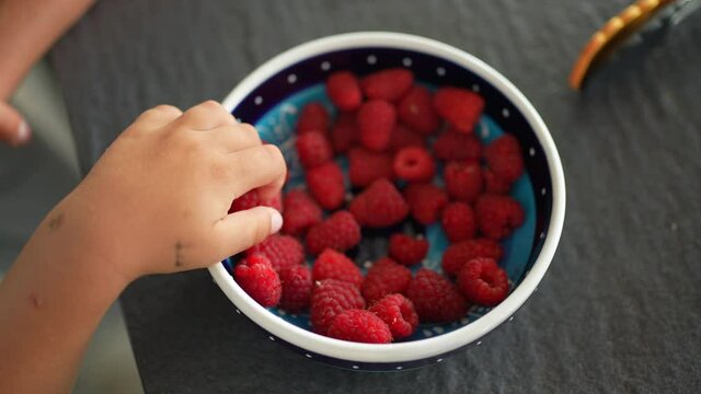 Hand grabbing raspberry fruit from bowl