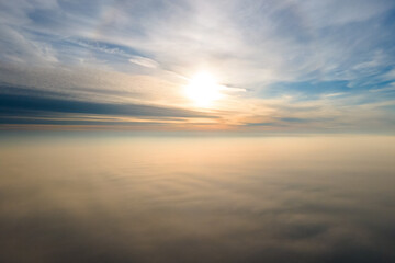 Naklejka na ściany i meble Aerial view of vibrant yellow sunrise over white dense clouds with blue sky overhead