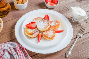 Delicious pancakes with strawberries and powdered sugar on a white plate on a dark wooden plate