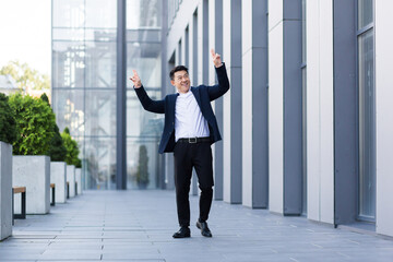Fototapeta na wymiar Happy smiling and successful Asian businessman dances with pleasure and good result of his work