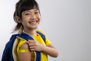  Asian young girl showing her arm with yellow bandage after got vaccinated or inoculation, child...