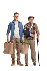 Young man helping an elderly man with a broken arm and carrying grocery shopping bags