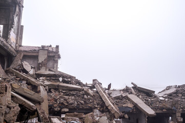 Ruins of concrete fragments of a destroyed building in a hazy haze against a gray sky. Background