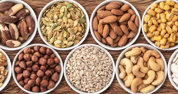 Assorted nuts and seeds in bowls over wooden table, panoramic format