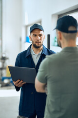 Fototapeta premium Foreman of auto repair shop uses laptop and talks to a mechanic in workshop.