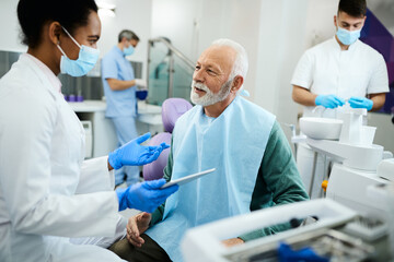 Naklejka na ściany i meble Happy senior man talks to his dentist during teeth check-up at dental clinic.