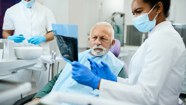 Senior man and his dentist analyse dental X-ray during appointment at dentist's office.