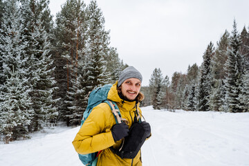 Fototapeta na wymiar Smiling and happy traveler with hiking backpack on the back. Snowy forest and rocks. Climbing the mountain in winter. Survival in the wild.