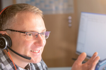 Mann mit Headset telefoniert in seinem Büro mit Lächeln im Gesicht