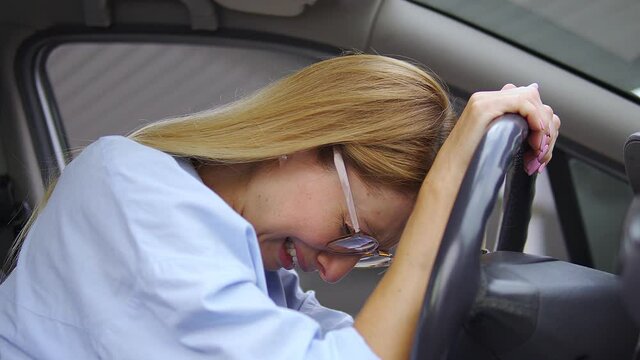 Female driver frowning face and crying sitting in car, leaning head on steering wheel, lost on road, run out of fuel and feeling confused and scared, receiving traffic ticket, road accident