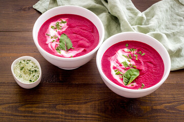 Two white bowls of red beet soup with sour cream and green herbal salt