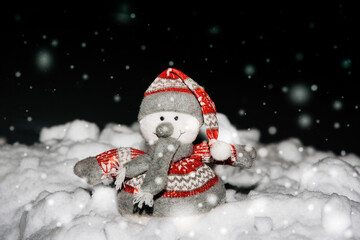 Toy snowman against the background of a dark Christmas night sky and snow