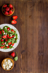 White plate of green spinach salad with strawberry and goat cheese
