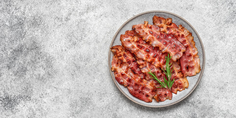 Fried bacon in a plate on a gray grunge background. Top view, flat lay, banner.