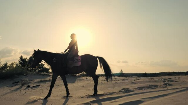 Horse riding. Silhouette of rider and horse. horsewoman is riding a horse on sandy ground, at sunset, against sun backlight and sky background. Equitation.