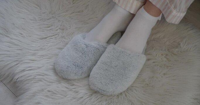 Young woman putting on soft slippers in morning