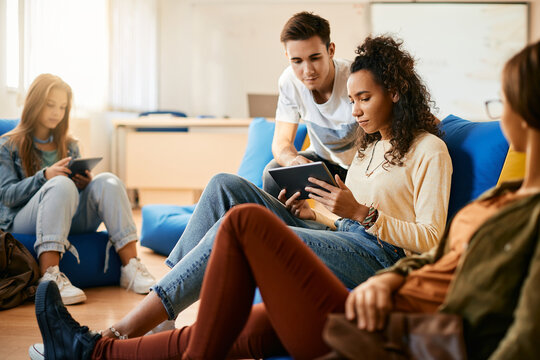 Black teenage girl uses digital tablet while having break with her classmates in classroom.