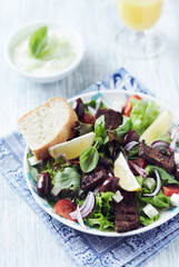 Salad with Grilled Beef Pieces, Cherry Tomatoes, feta Cheese and Kalamata Olives. Bright wooden background. Close up.