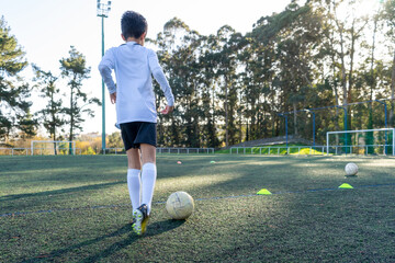 Child with his back to a soccer practice on a sunny day on an artificial turf field. Colored cones demarcating the practice to improve the use of the ball. Concept of sport for children. High quality