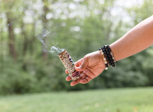 A woman hand holding buring sage and beads in the wrist