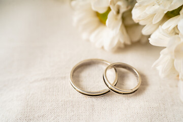 Pair of wedding rings on a white surface with beautiful white flowers. Commitment and love concept....