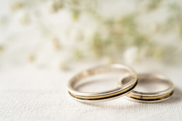 Obraz na płótnie Canvas Pair of wedding rings on a white surface with beautiful white flowers. Commitment and love concept. Copy Space, differential focus.