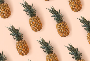 A bright pattern of many pineapples on a trendy soft beige pink background. Tropical ripe juicy fruit flat lay for your design projects