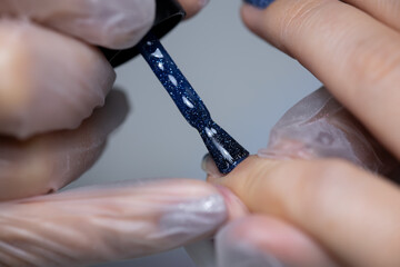 the manicure master performs the final stage of applying gel polish to the nail surface with a brush