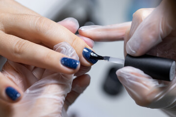 Obraz na płótnie Canvas close-up, the master evens the color of the manicure with blue, applying gel polish on it with a brush