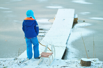 Fototapeta Child with a sled on a frozen lake. Dangerous fun on thin ice in winter. obraz