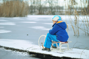 Child with a sled on a frozen lake. Dangerous fun on thin ice in winter.