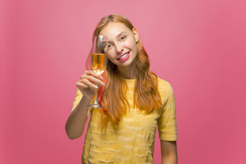 Beautiful happy female celebrating holiday holding glass of champagne, smiling, congratulating on pink studio background