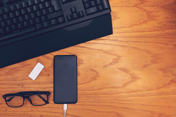 Workplace. On a wooden table are located: keyboard, glasses, smartphone and card reader.