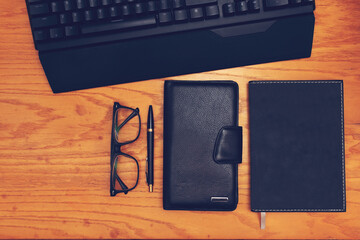 Workplace. On a wooden table are located: keyboard, glasses, pen, notebook and card holder.