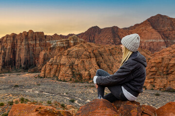 Contemplative Woman sitting on a rock ledge overlooking beautiful Snow Canyon State park in the deserts of Utah enjoying the view