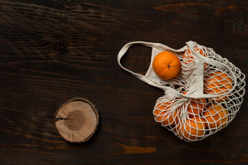 Fresh mandarin oranges fruit or tangerines on a wooden table. Christmas composition. Mandarin oranges in organic cotton mesh bag. Grocery shopping fabric net bag. No plastic bag. - 477521729
