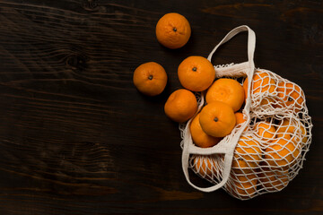 Fresh mandarin oranges fruit or tangerines on a wooden table. Christmas composition. Mandarin oranges in organic cotton mesh bag. Grocery shopping fabric net bag. No plastic bag. - 477521742