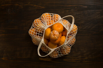 Fresh mandarin oranges fruit or tangerines on a wooden table. Christmas composition. Mandarin oranges in organic cotton mesh bag. Grocery shopping fabric net bag. No plastic bag. - 477521789