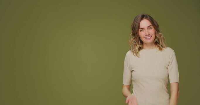 Smiling friendly young woman waving hand, greeting, welcoming, invite to come in showing copy space for advertisement