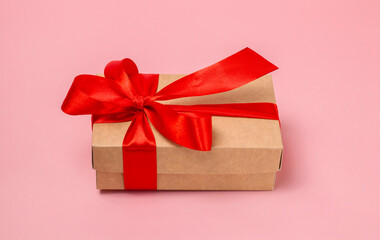 A gift for a loved one in a craft box tied with a red satin bow on a pink background.