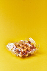  Single delicious waffle wrapped on plastic bag over yellow background