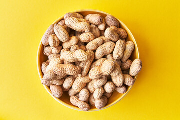  Bowl of peanuts with shell on a yellow background