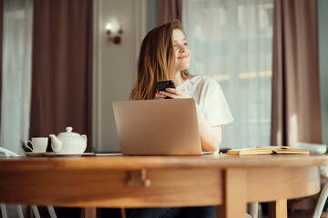 Young female student online studying at home remotely. A freelancer surfs the Internet searching for video webinars. The designer is working on a laptop in the workplace room.