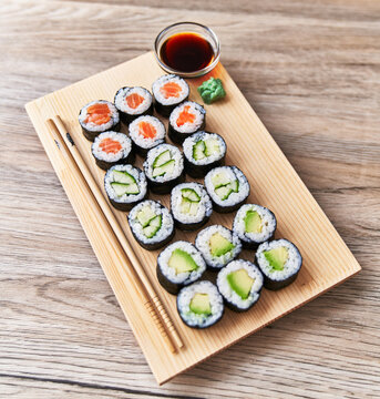  Wooden board with avocado, salmon and cucumber sushi makis on a wooden surface