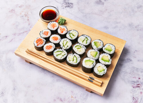  Wooden board with avocado, salmon and cucumber sushi makis on a marble surface