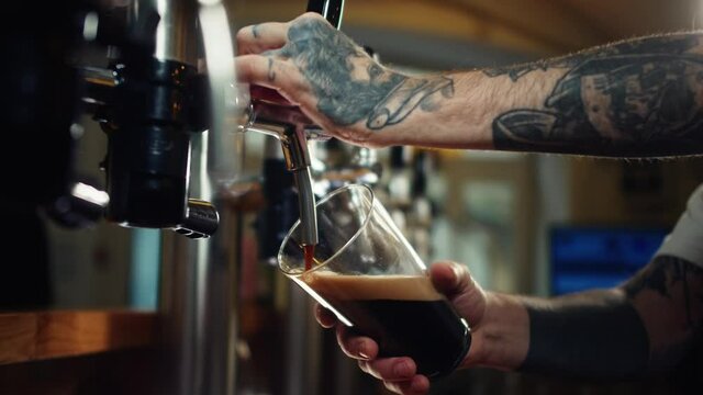 Barman pouring nitrogen beer into glass close-up. Bartender pours alcohol foamy drink in mug. Fresh beverage on bar counter background in pub.