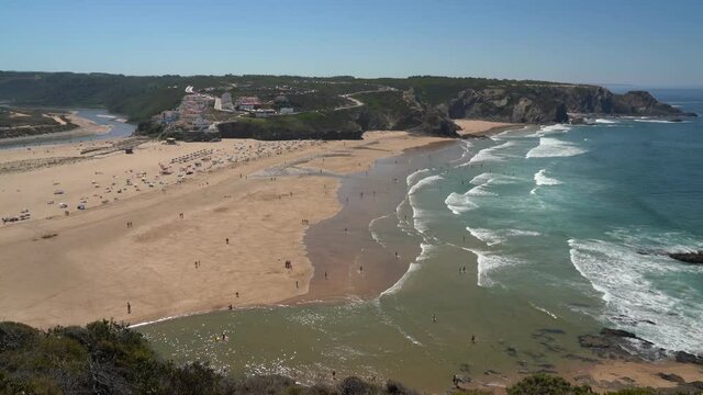 Filming the beautiful bay in the Portuguese town of Odeceixe in the summer with tourists on the beach.