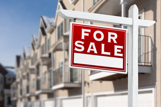 For Sale Real Estate Sign In Front of a Row of Apartment Condominiums Balconies and Garage Doors.