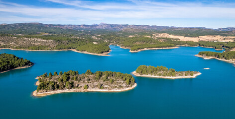 island with green trees sun over water reflection islet blue water vegetation shore aerial view drone photography horizon with mountains sunny blue sky