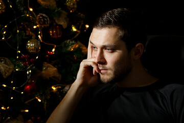A tired man, lost in thought, sits by the New Year tree. New year's eve